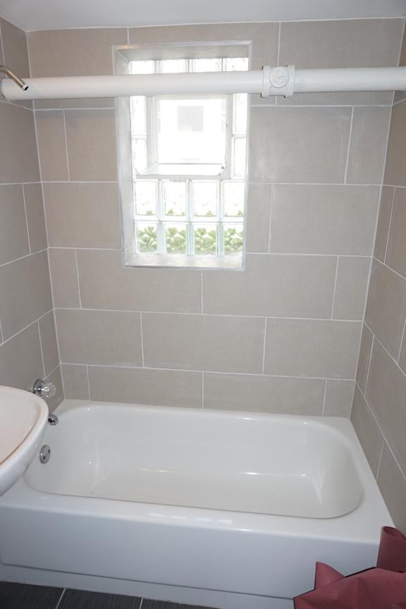 A white bathtub sits in a bathroom with a window above it.