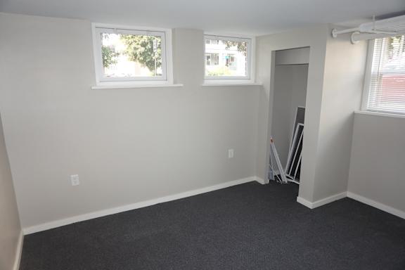 A room with a carpeted floor, two windows, and a door with a ladder in it.