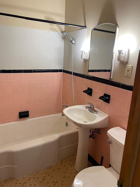 A white sink is on a pedestal in a pink tiled bathroom.