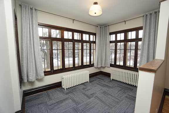 A room with a grey carpet and a window with curtains.