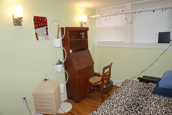 A room with a bed, a chair, a cabinet, and a plant.