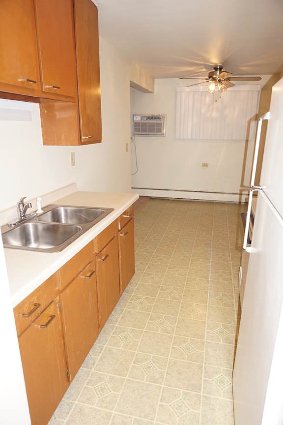 A kitchen with a white fridge, brown cabinets and a ceiling fan.