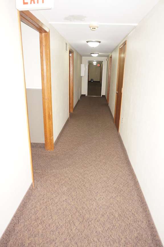 A long hallway with a door on the left and an exit sign on the ceiling.