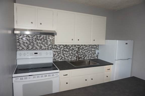 A kitchen with white cabinets and a black and white tiled backsplash.
