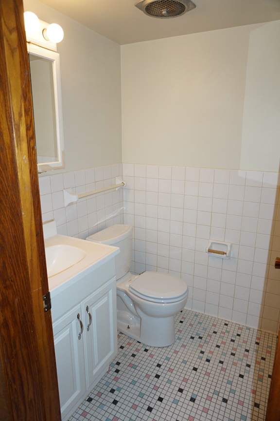 A white toilet sits in a bathroom with a sink and a mirror.