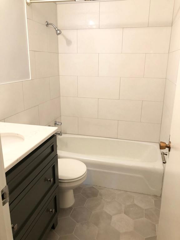 A white tiled bathroom with a toilet and a bathtub.