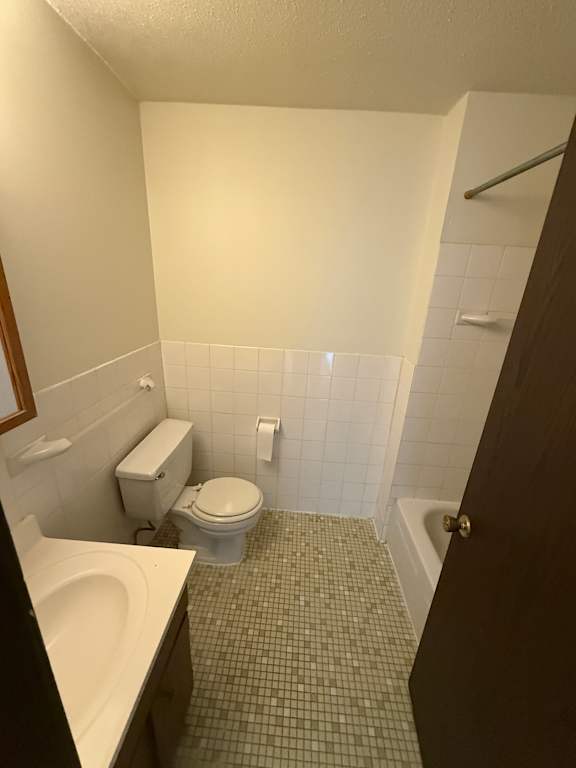A white toilet sits in a bathroom with a white tiled wall.