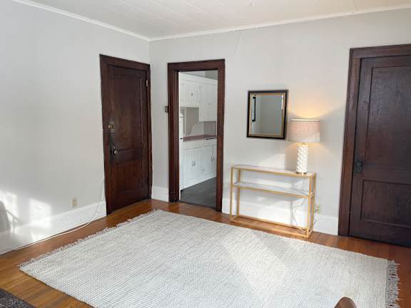 A white rug is on a wooden floor in a room with a mirror, lamp, and two doors.