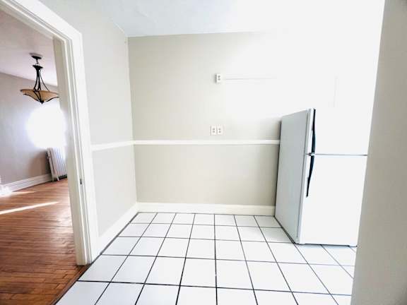 A white fridge in a room with white walls and a white tiled floor.