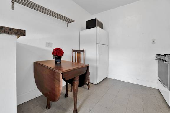 A wooden table with a red flower on it sits in a white room.