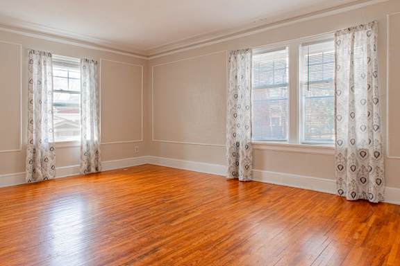 A room with wooden floors and two windows with curtains.