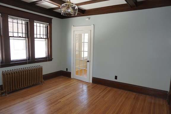 A room with a white door and a window with a radiator under it.