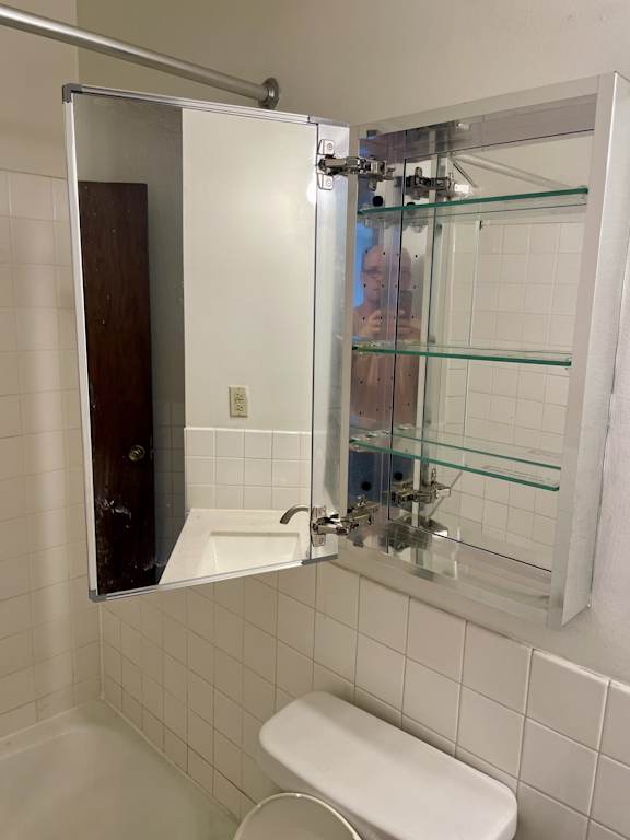 A white toilet sits in a bathroom with a white sink and a mirror.