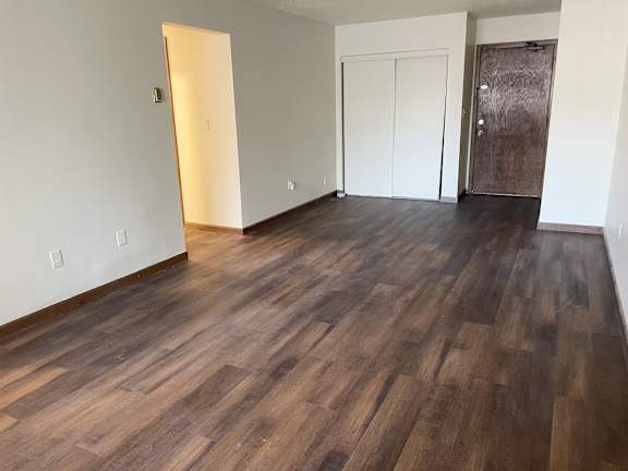 A room with wooden floors and a white wall with a door and a window.