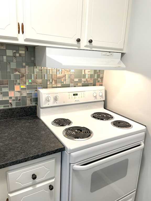 A white stove with a black stove top is in a kitchen with white cabinets.