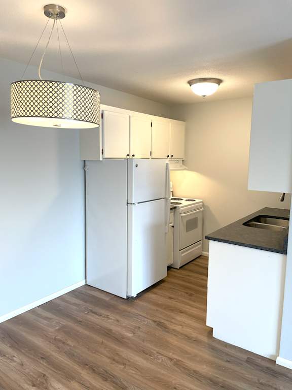 A kitchen with white appliances and wooden floors.