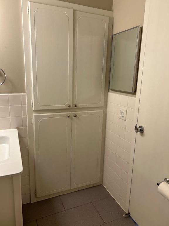 A white bathroom with a sink, toilet paper, and a shower.