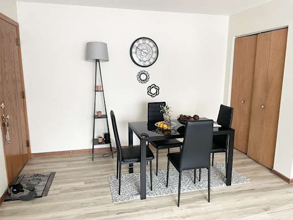 A black dining table with four chairs and a grey floor lamp.