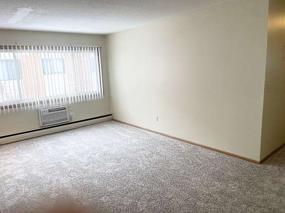 A room with a carpeted floor and a window with blinds.