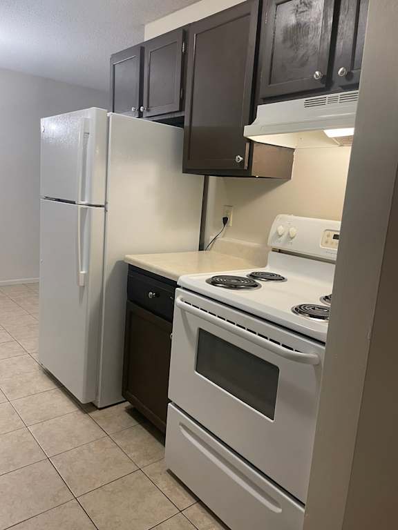 A white refrigerator stands next to a white stove in a kitchen.