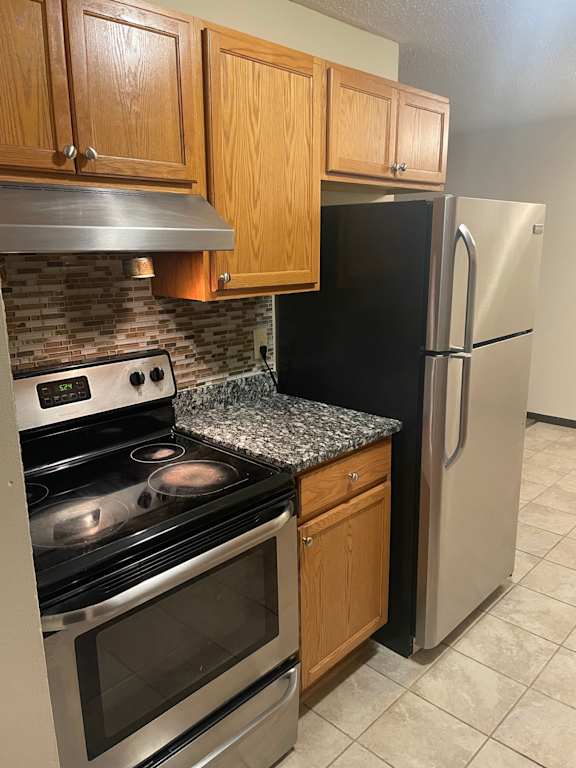 A kitchen with a stove, refrigerator, and cabinets.