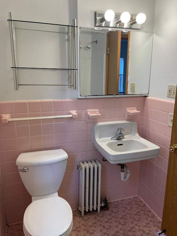 A white toilet sits next to a sink in a pink tiled bathroom.