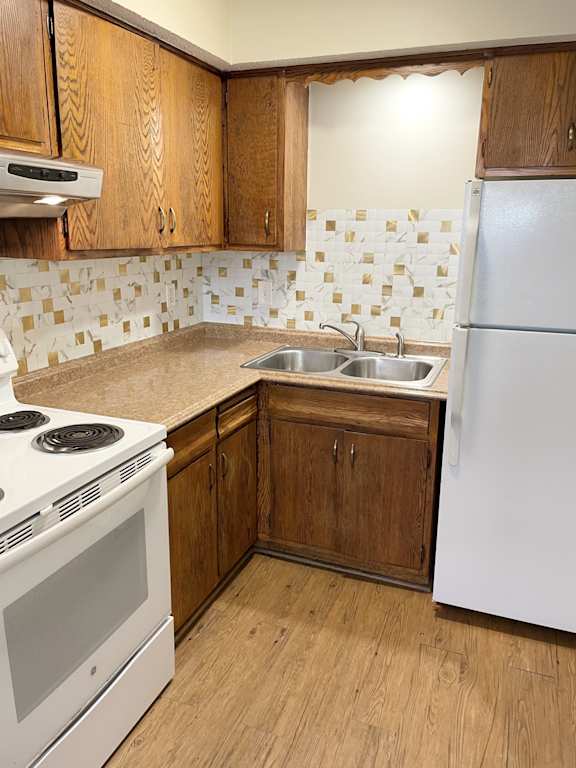 A kitchen with a white stove, white refrigerator, and wooden cabinets.