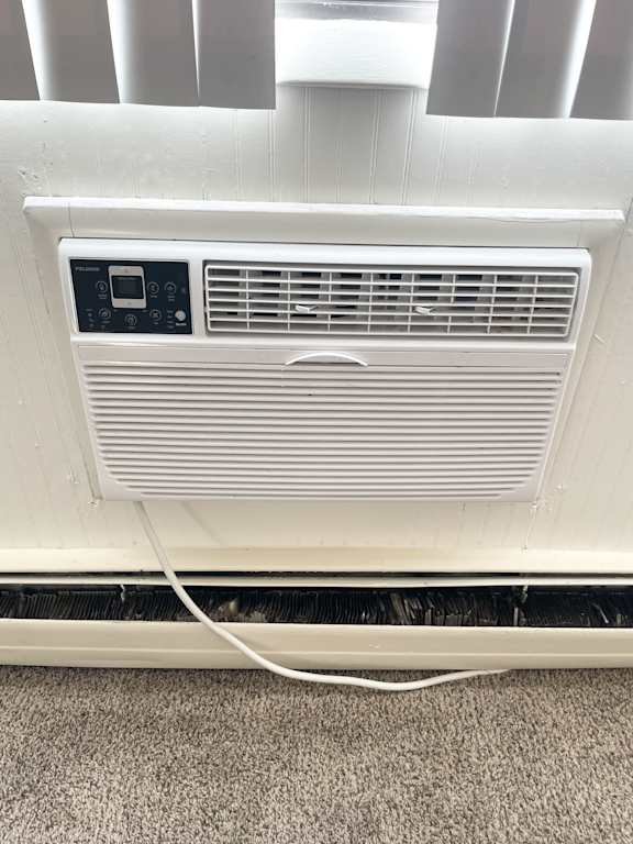 A white air conditioner unit with a remote control and a power cord plugged into the wall.