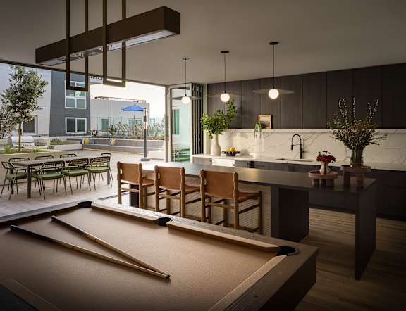 A pool table is in the middle of a room with a bar and chairs.