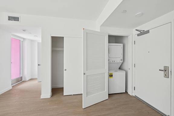 A white room with a pink door and a white fridge.