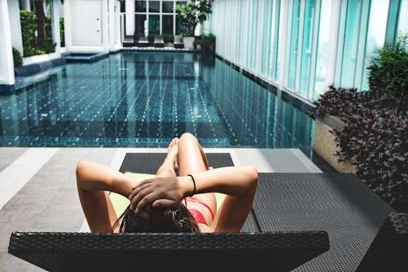 A woman in a red bikini is sunbathing on a lounge chair by a pool at Coro Apartments, Los Angeles
