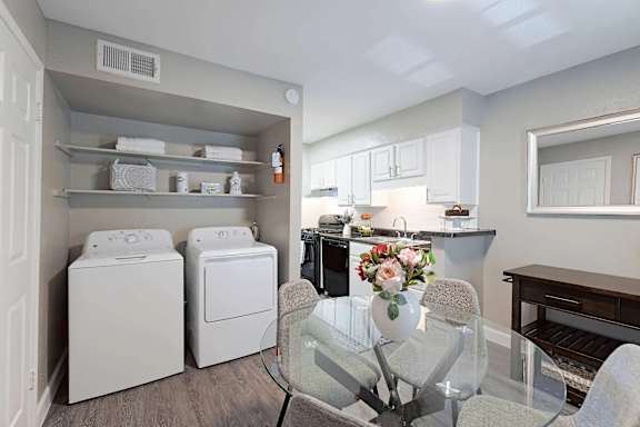 A laundry room with a washer and dryer, a dining table with chairs, and a kitchen area with cabinets and a countertop.
