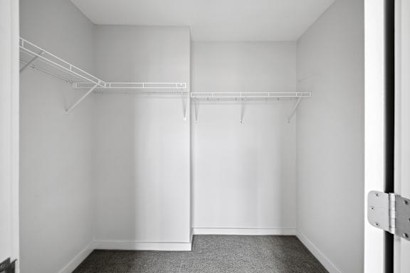 A white closet with a grey carpet and two white shelves.