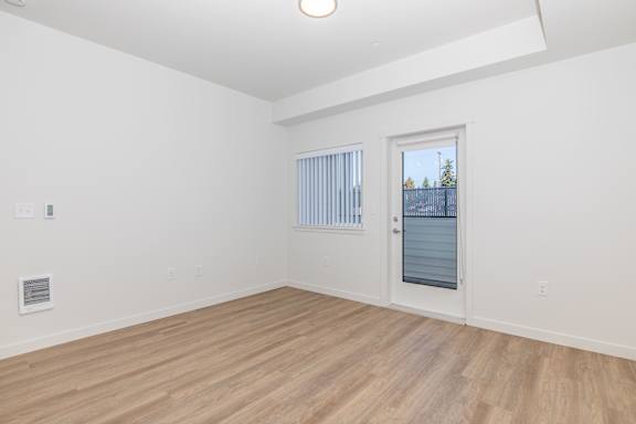 A room with a wooden floor and a window with a view of a fence and trees.