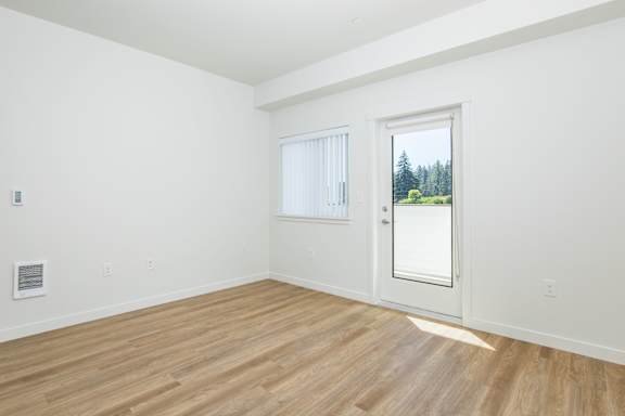 A room with a wooden floor and a door leading to a balcony with a view of trees.