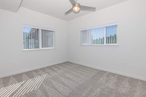 A room with a ceiling fan and two windows.