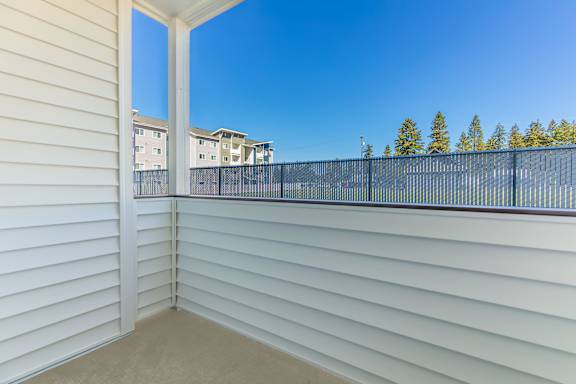 A balcony with white walls and a black railing overlooks a residential area.