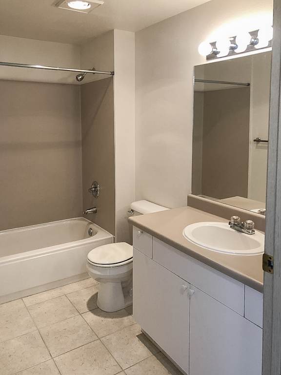 A white toilet sits in a bathroom next to a sink and a bathtub.