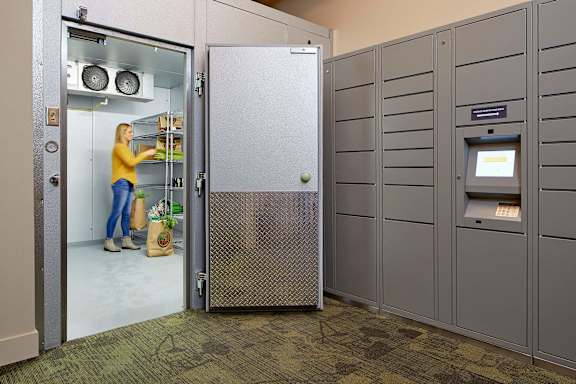 A woman is standing in a kitchen area with a refrigerator, oven, and microwave.