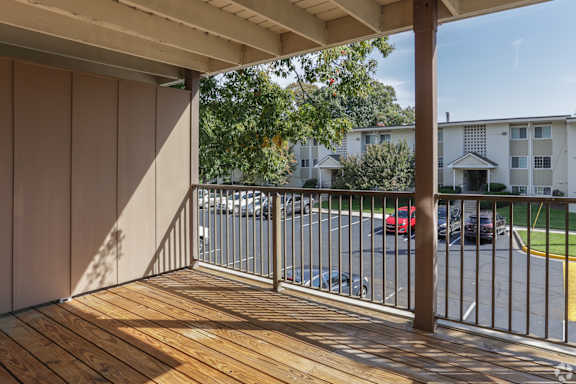 A balcony with a wooden floor and metal railing overlooking a parking lot.