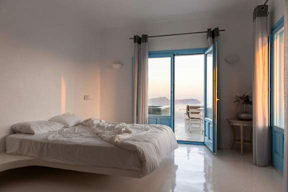 A bedroom with a large bed and a view of the ocean through the open door.