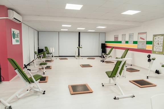 A gym with green chairs and exercise equipment.