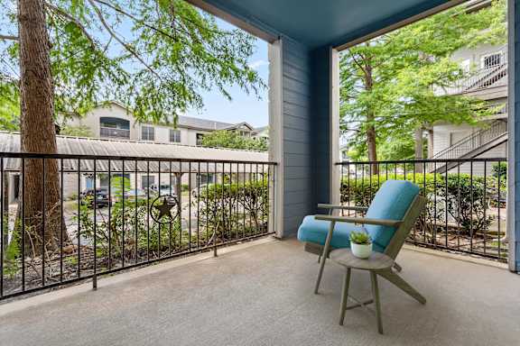 A chair sits on a patio with a view of a street and houses.