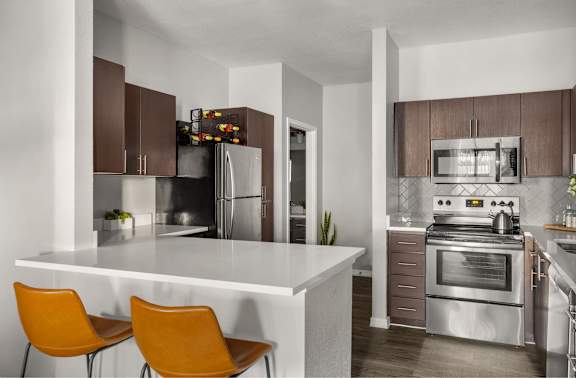 A modern kitchen with a white island and orange chairs.