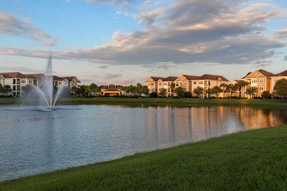 A fountain in the middle of a lake with houses in the background.