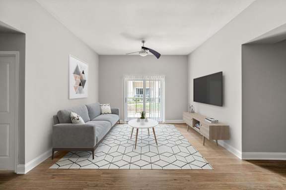 A living room with a grey couch, a white rug, and a ceiling fan.