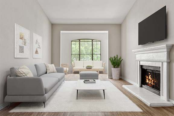A living room with a grey couch, a coffee table, a fireplace, and a flat screen TV mounted on the wall.