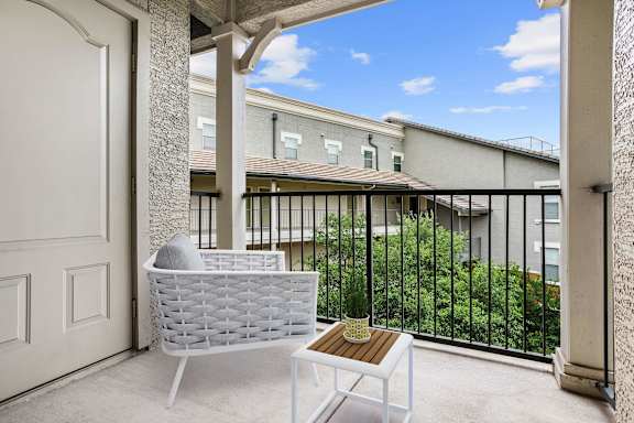 A white chair and table are on a patio with a view of a building and trees.