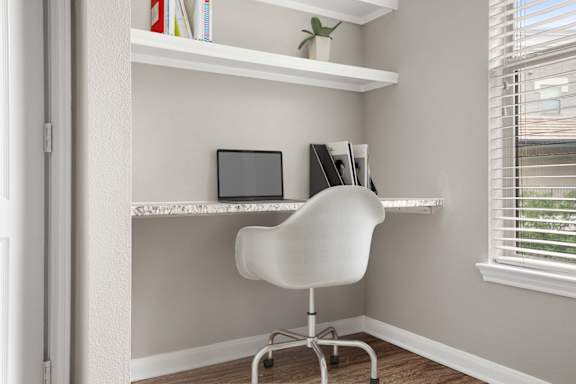 A white chair is in front of a desk with a laptop and a plant on it.