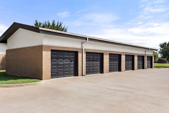 A building with a brown brick facade and a white roof has four black garage doors.